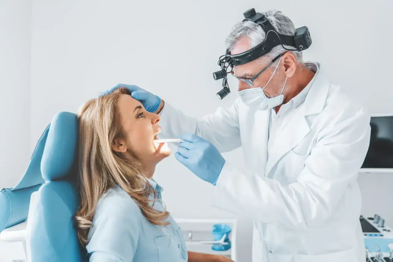 Lekarz bada jamę ustną pacjentki. Czy z afta można iść do dentysty? Tak, dentysta pomoże ocenić problem.
