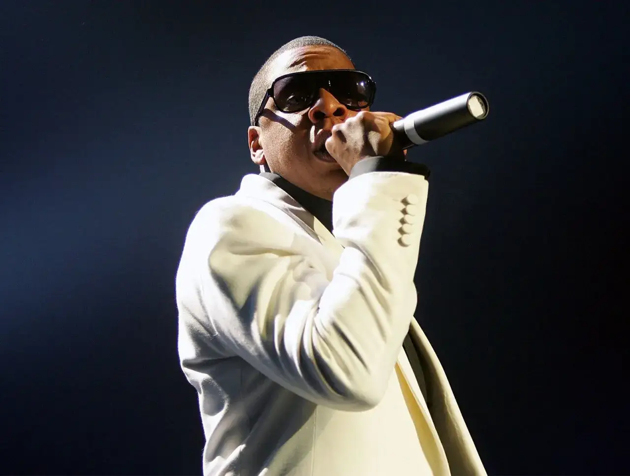 Jay-Z w białej marynarce i okularach przeciwsłonecznych śpiewa do mikrofonu. Jego majątek robi wrażenie.