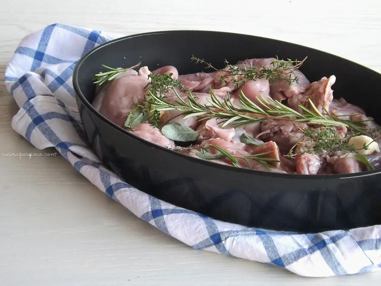 Coniglio crudo in teglia con rosmarino, salvia e aglio, pronto per scoprire come cucinare il coniglio.