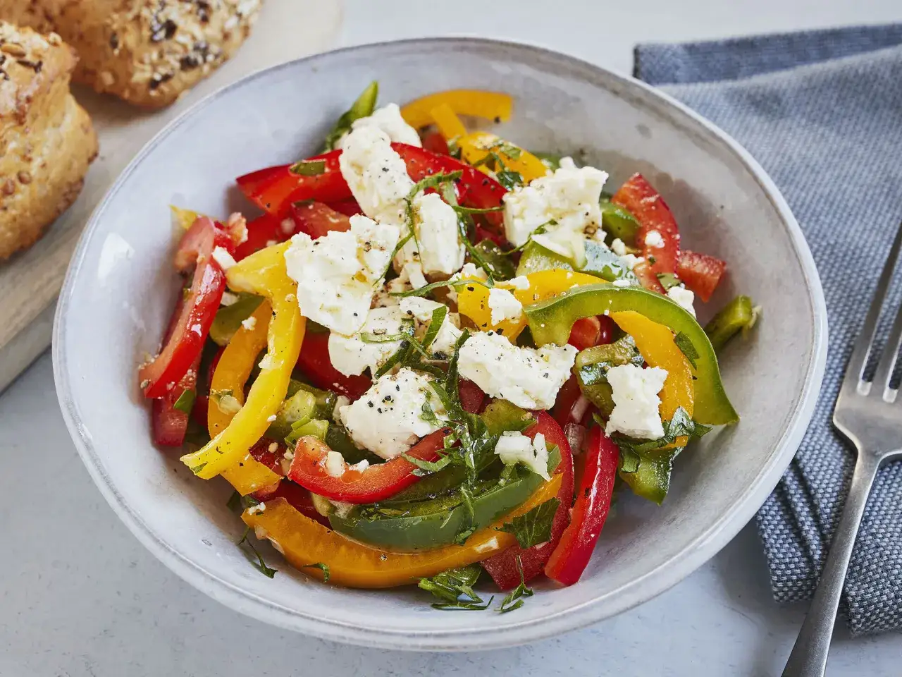 Bunter Paprikasalat mit Feta, garniert mit frischen Kräutern und schwarzem Pfeffer. Dazu passen knusprige Brötchen.