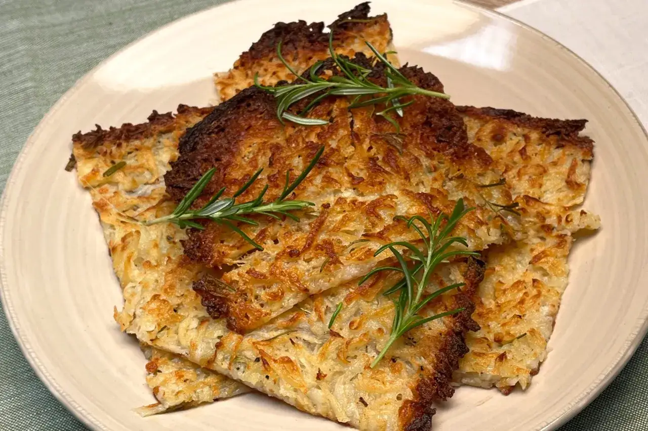 Rosti di patate dorati e croccanti, guarniti con rametti di rosmarino fresco, serviti su un piatto chiaro.
