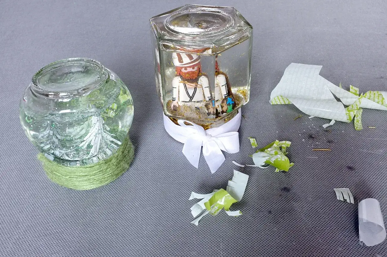Dwa słoiki z brokatem i figurkami, jeden z nich to kula śnieżna diy z ludzikiem.