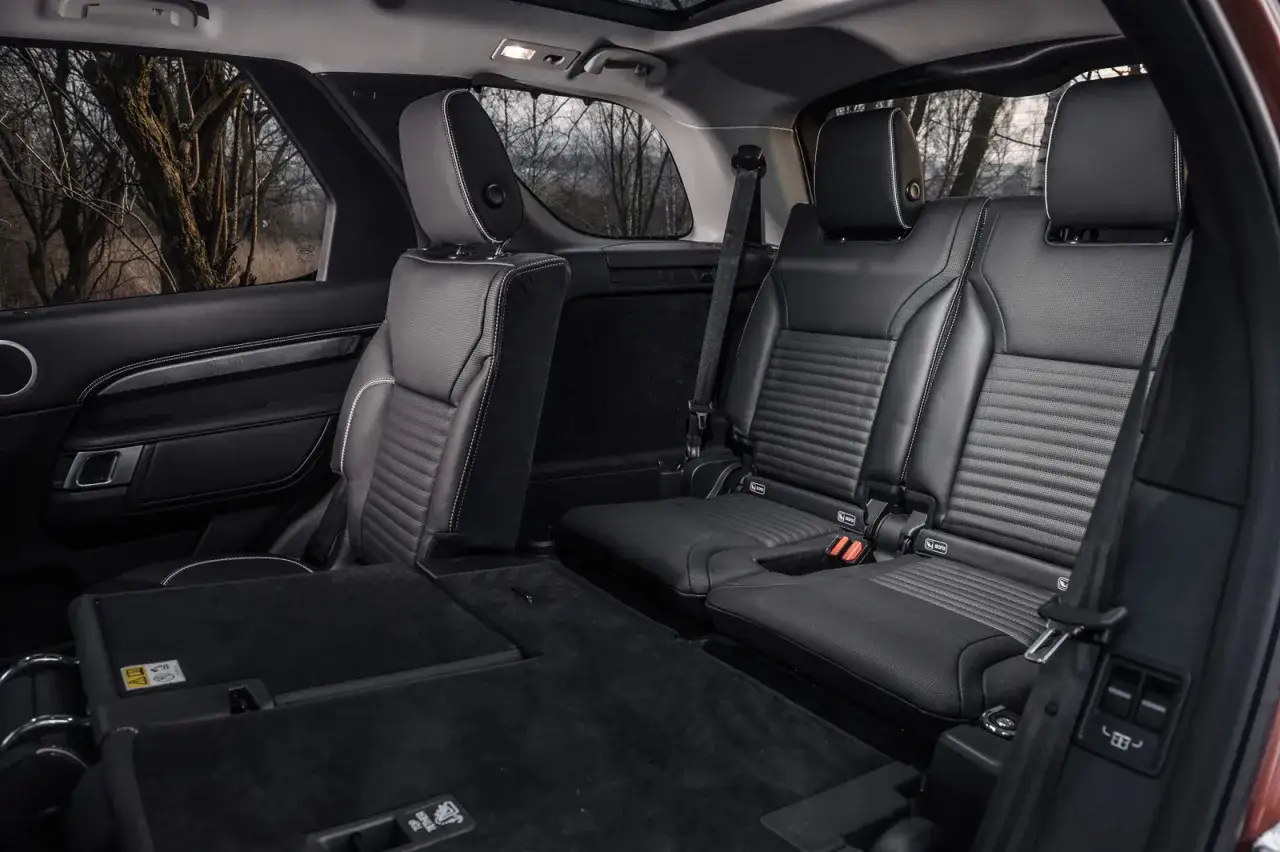 Wnętrze Land Rover Discovery 5 z czarnymi, skórzanymi siedzeniami i złożonymi tylnymi siedzeniami, gotowe na przygodę.