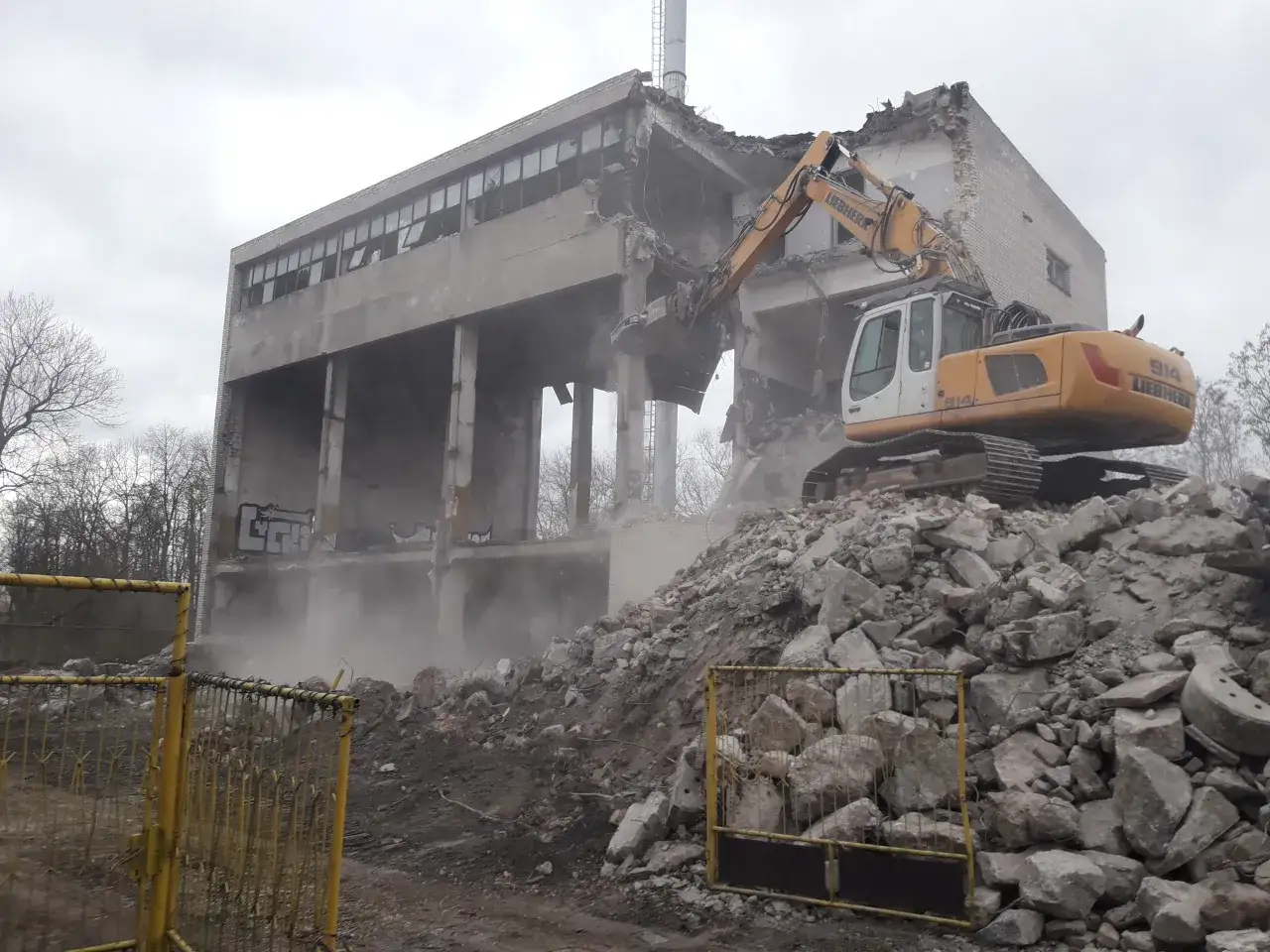 Żółty koparka Liebherr burzy betonowy budynek, tworząc stertę gruzu. Trwa wyburzanie, a cena za m3 jest kluczowa dla tego procesu.