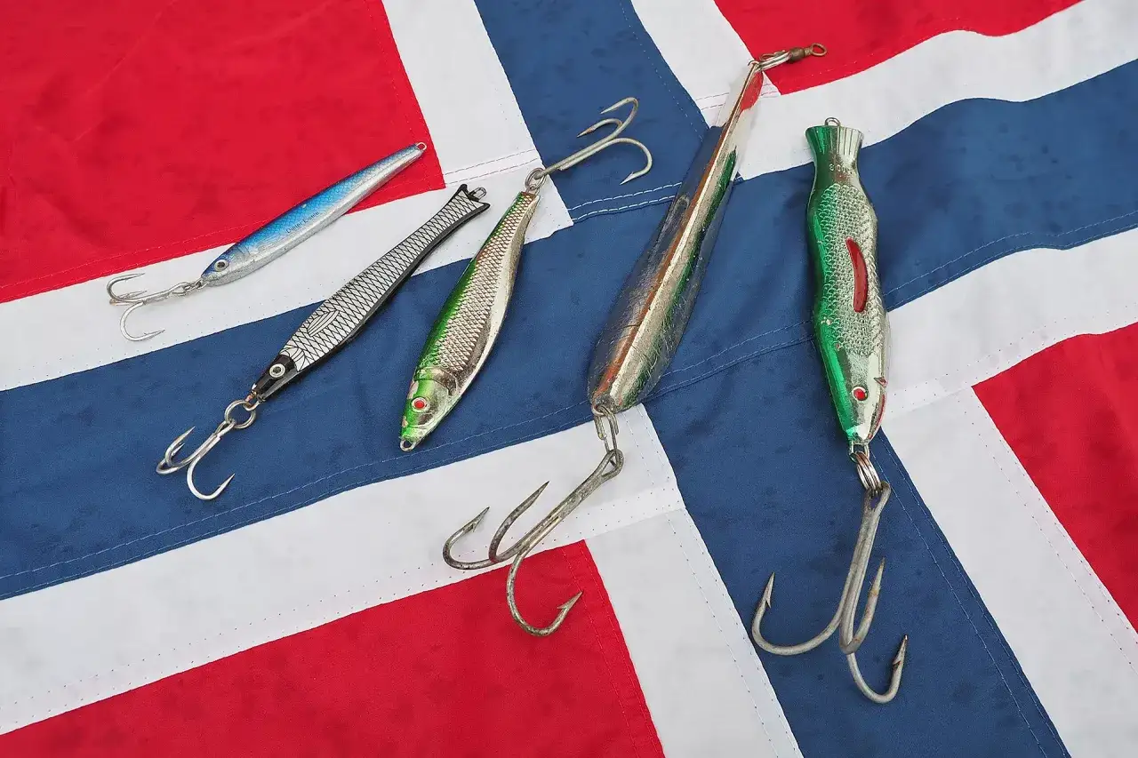 F&uuml;nf Pilker und Haken liegen auf einer norwegischen Flagge. Bereit f&uuml;r das Pilken vom Ufer.