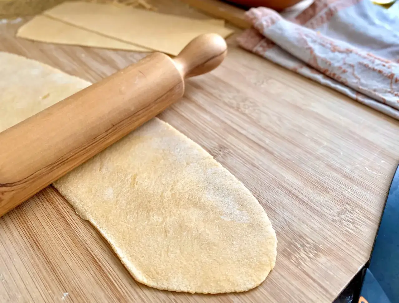 Holzrolle auf Teig f&uuml;r italienische Pasta selber machen. Mehrere Teigplatten liegen bereit.