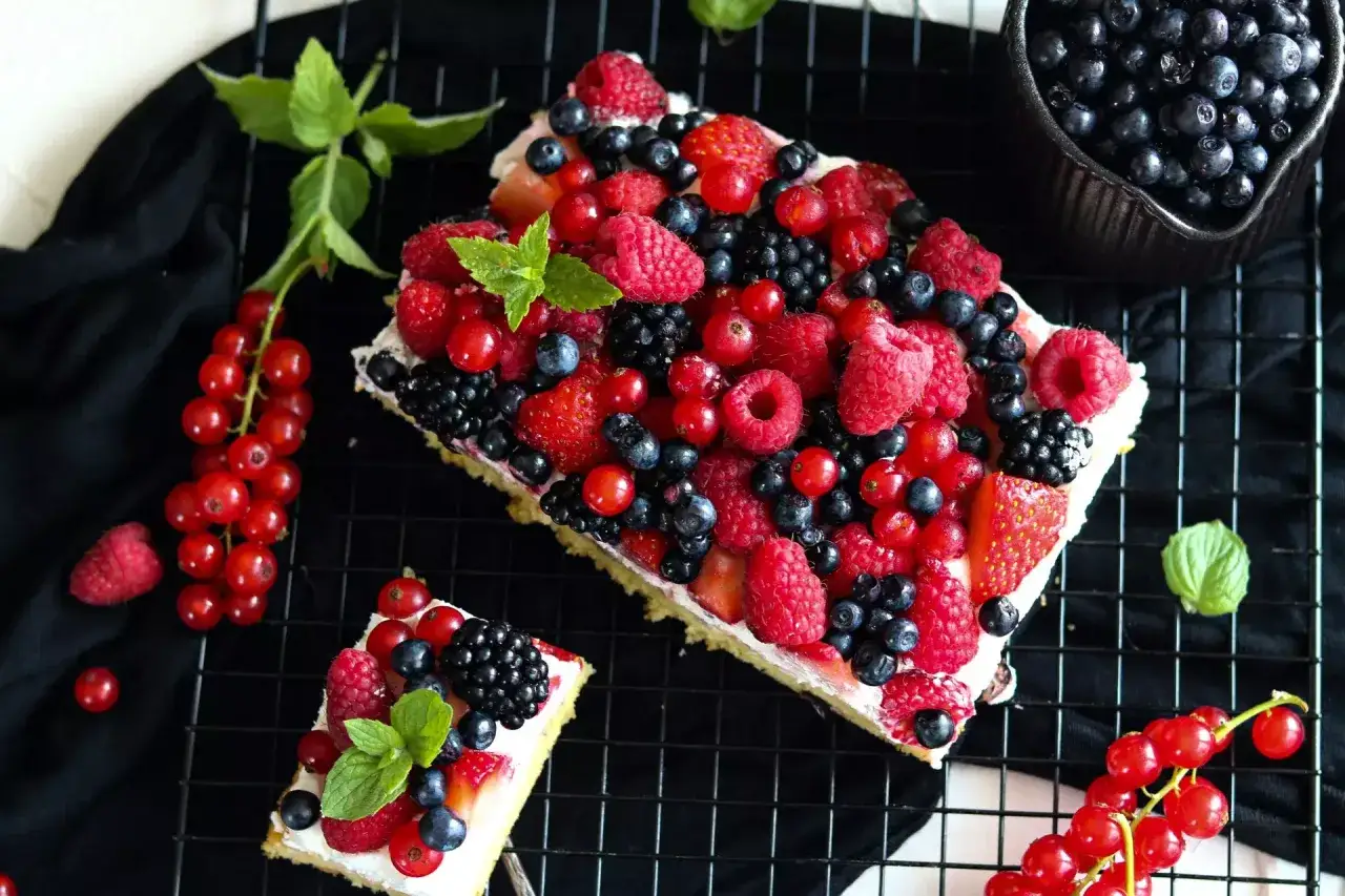 Ein köstlicher Beerenkuchen vom Blech, üppig belegt mit frischen Himbeeren, Blaubeeren, Johannisbeeren und Erdbeeren.