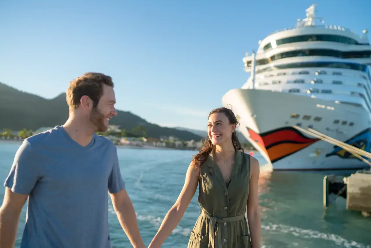 Gl&uuml;ckliches Paar h&auml;lt H&auml;ndchen vor AIDA Schiff. Perfekt f&uuml;r die Packliste Kreuzfahrt AIDA.