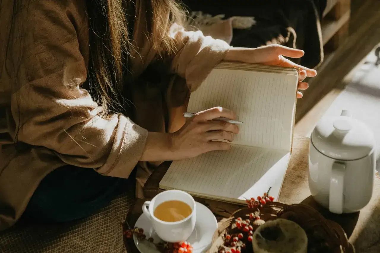 En person skriver i en anteckningsbok under en 5 minute meditation. En kopp te och en tekanna står bredvid.