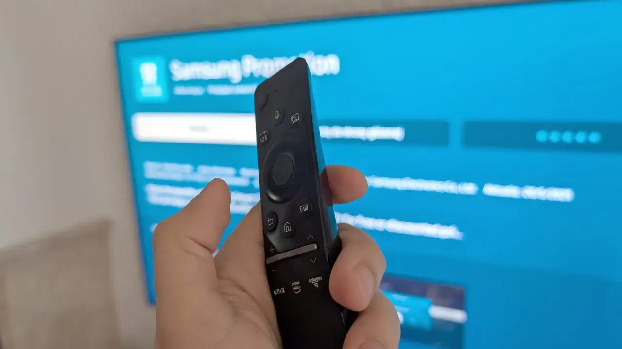 Dłoń trzymająca pilot do telewizora Samsung, ekran pokazuje menu, jak wgrać aplikacje do telewizora.