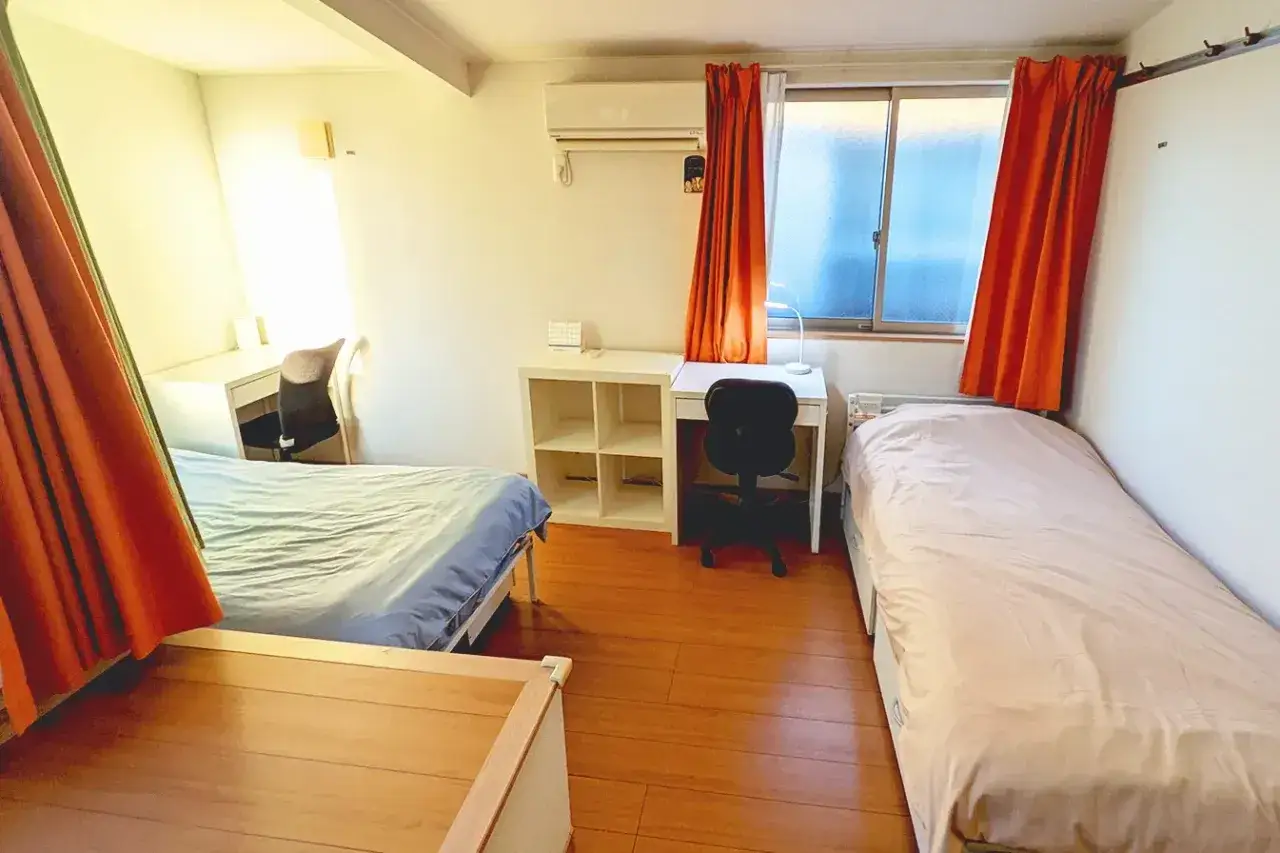 Chambre d'étudiant à Tokyo avec deux lits, bureaux et étagères.
