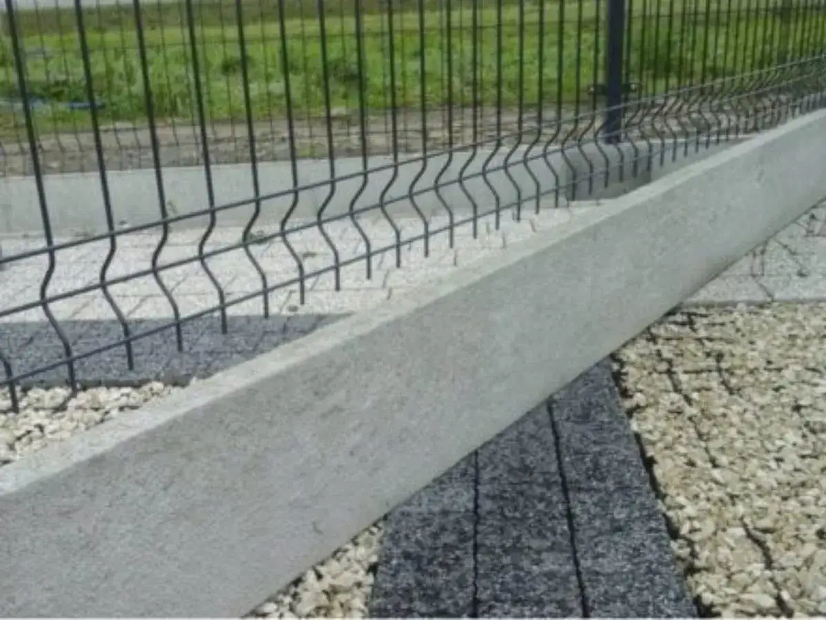 Solidna podmurówka betonowa pod siatką ogrodzeniową, zabezpieczająca przed przerastaniem trawy i zwierzętami.