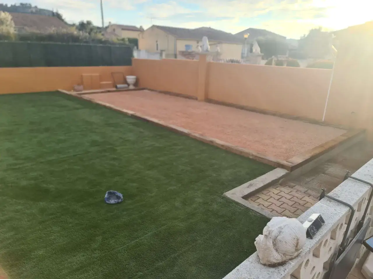 Un terrain de p&eacute;tanque pr&ecirc;t pour l'entretien, avec une pelouse synth&eacute;tique et un espace de jeu en gravier.