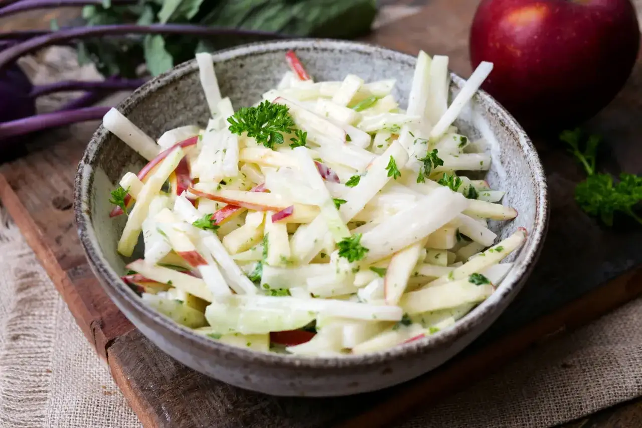 Ein cremiger Kohlrabi-Salat mit Apfelstücken und frischer Petersilie, garniert mit einem Apfel.