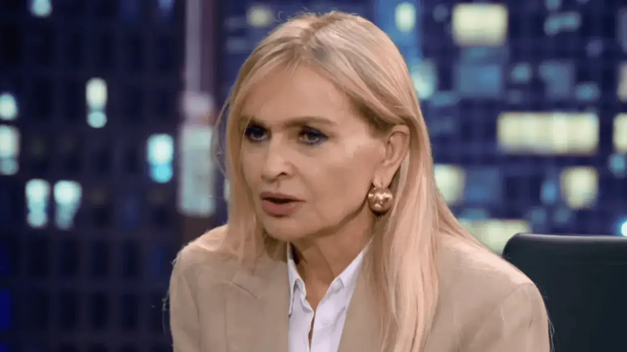 Monika Olejnik w beżowej marynarce i białej koszuli, z dużymi złotymi kolczykami. W tle nocne miasto.
