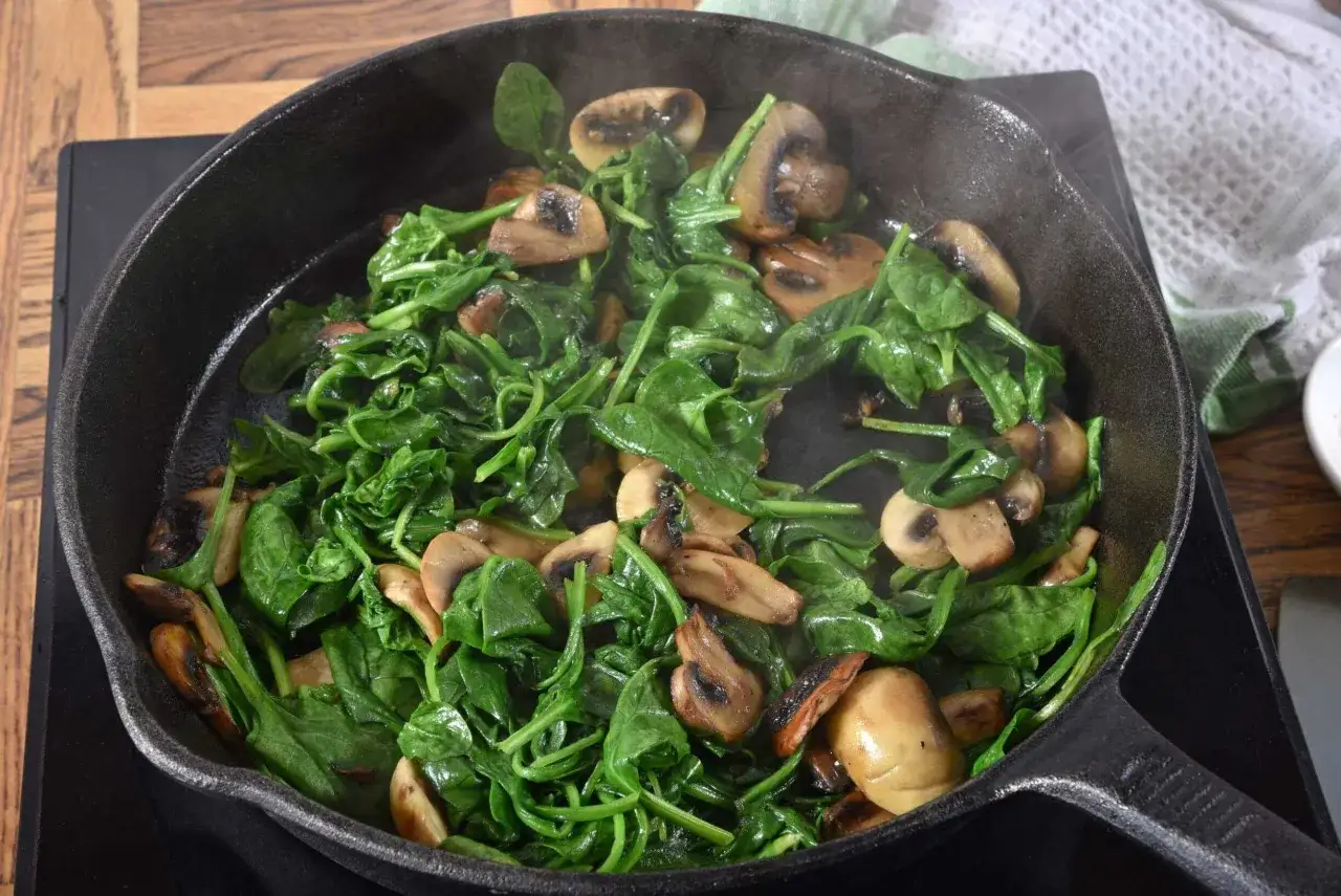 Baby Spinat Rezepte: Frischer Spinat und Pilze brutzeln in einer Gusseisenpfanne. Ein schnelles und gesundes Gericht.
