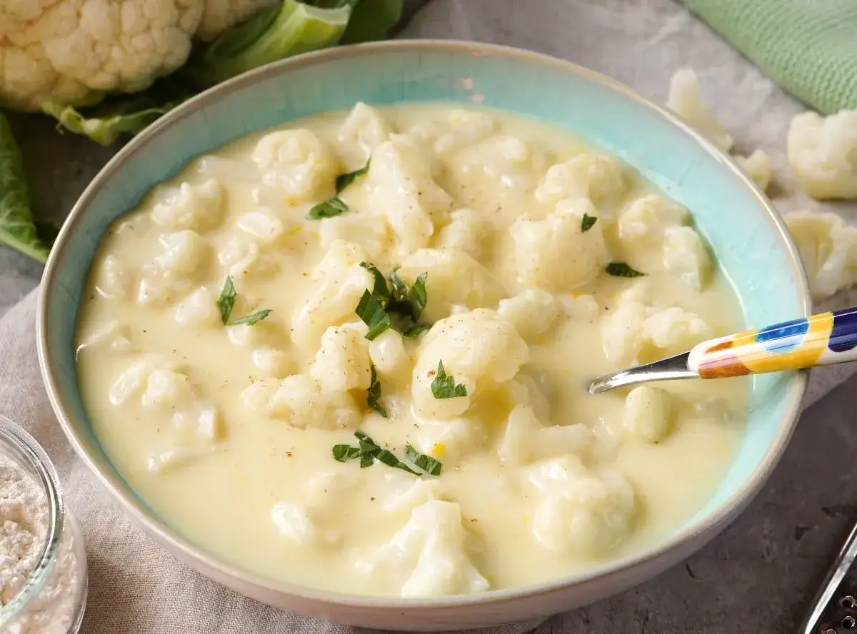 Cremige blumenkohlsuppe thermomix ohne kartoffeln, garniert mit Petersilie. Ein L&ouml;ffel mit buntem Muster liegt in der Sch&uuml;ssel.