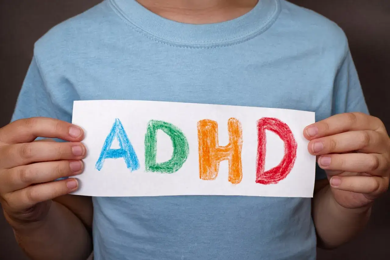 Dziecko trzyma kartkę z napisem ADHD, symbolizującym problemy z koncentracją.
