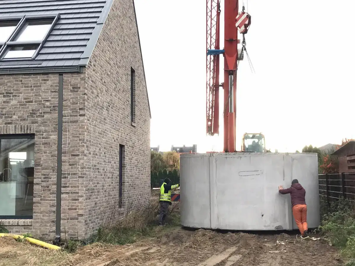 Montaż zbiornika na deszczówkę: dźwig opuszcza betonowy krąg, pracownicy pomagają w precyzyjnym ustawieniu.