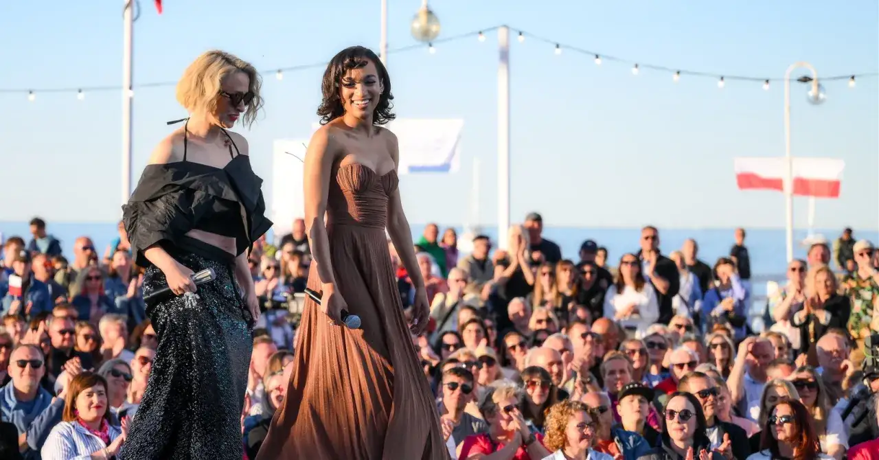 Dwie artystki na scenie podczas sopockich imprez na molo. Tłum widzów, polskie flagi i światła tworzą atmosferę letniego festiwalu.