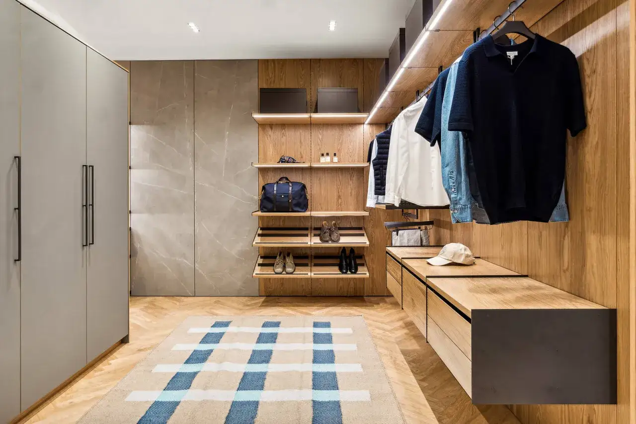 En walk-in-closet med trädetaljer, kläder på galgar och en matta. En känsla av quiet luxury.