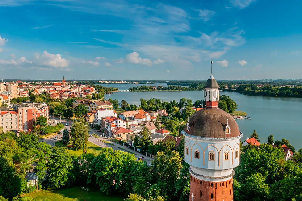 Widok na miasto z wieżą ciśnień i zielone jezioro w tle.