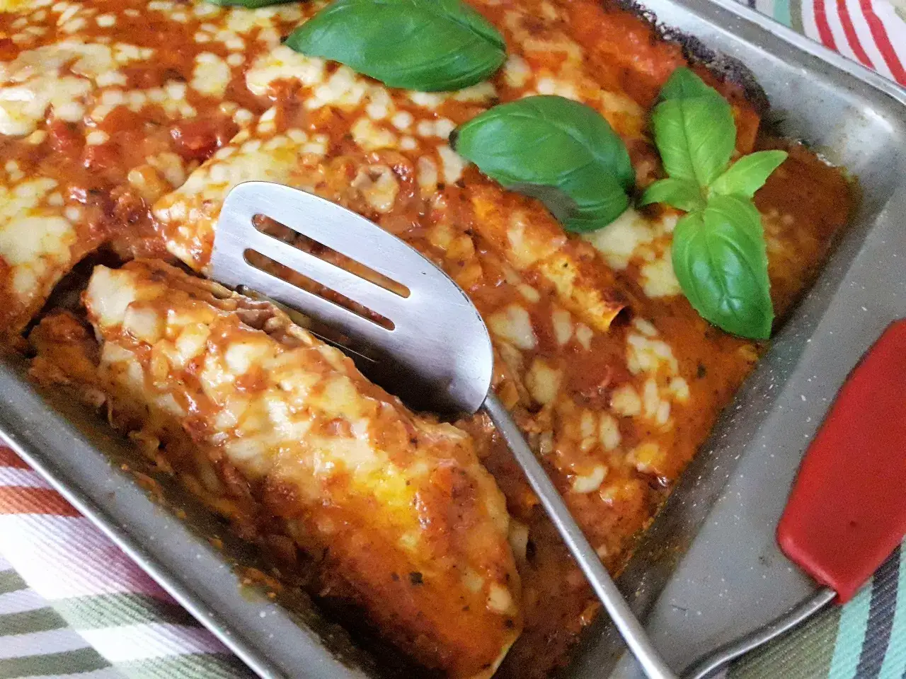 Pyszna tortilla z mięsem mielonym i serem, zapieczona w sosie pomidorowym, ozdobiona listkami bazylii.