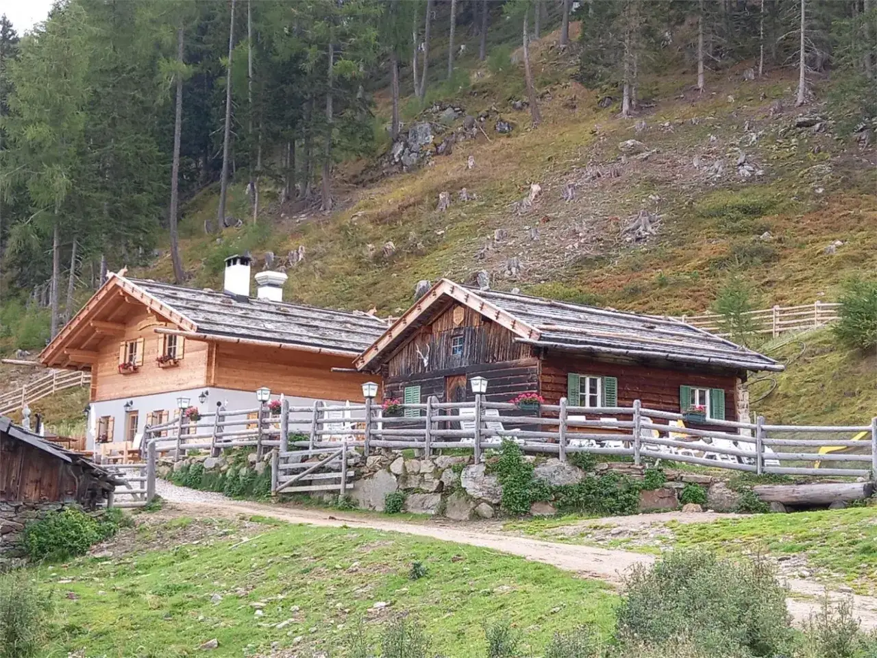 Tablander Alm a Parcines, con due baite in legno e recinzione, immerse nel verde di un pendio boscoso.