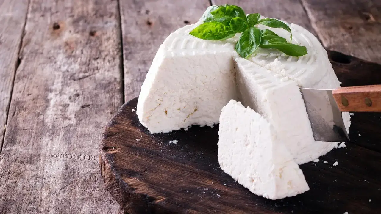 Un fromage frais, garni de basilic, est coupé sur une planche en bois. On dirait qu'il est temps de boire du petit lait.