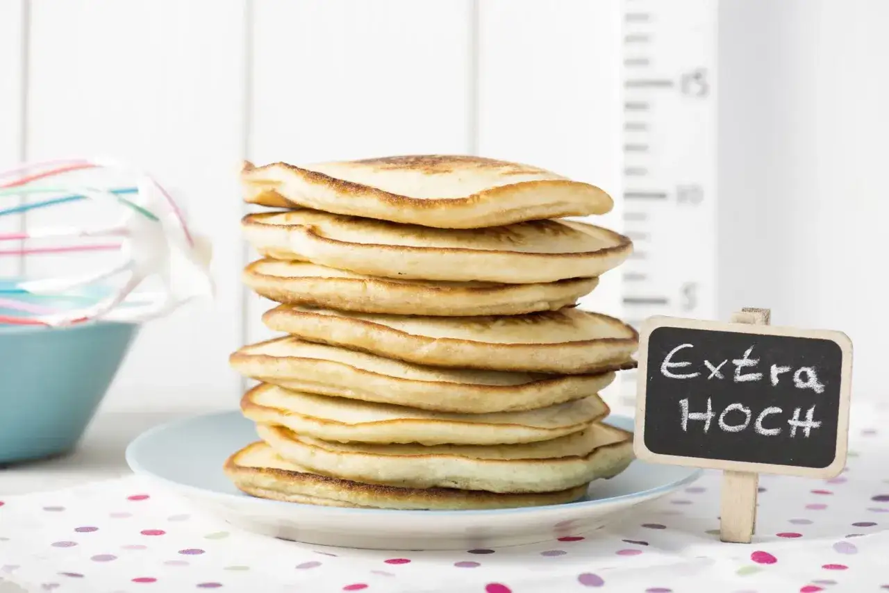 Ein Stapel fluffiger Pfannkuchen, die wie ein Turm aussehen. Ein kleines Schild sagt 