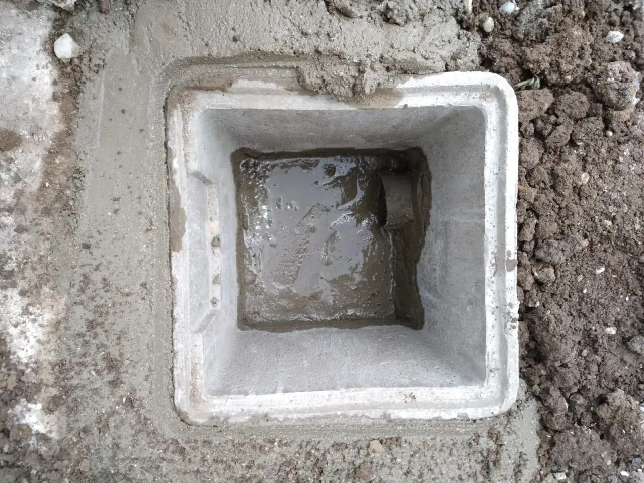 Un regard de b&eacute;ton fra&icirc;chement pos&eacute;, rempli d'eau pluviale. Le sol environnant est meuble et terreux.