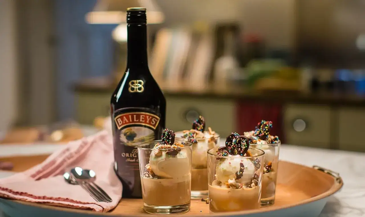 Baileys z czym pić? Idealnie z lodami i czekoladowymi dodatkami. Butelka Baileys obok deserów zachęca do degustacji.