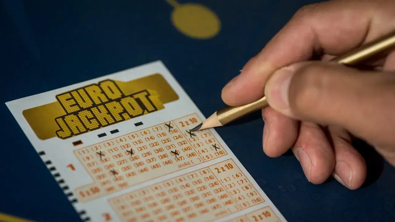 Dłoń z ołówkiem zaznacza liczby na kuponie Eurojackpot. Zastanawiasz się, dlaczego zwycięzca 206 milionów ze śląska nie odebrał nagrody od razu?