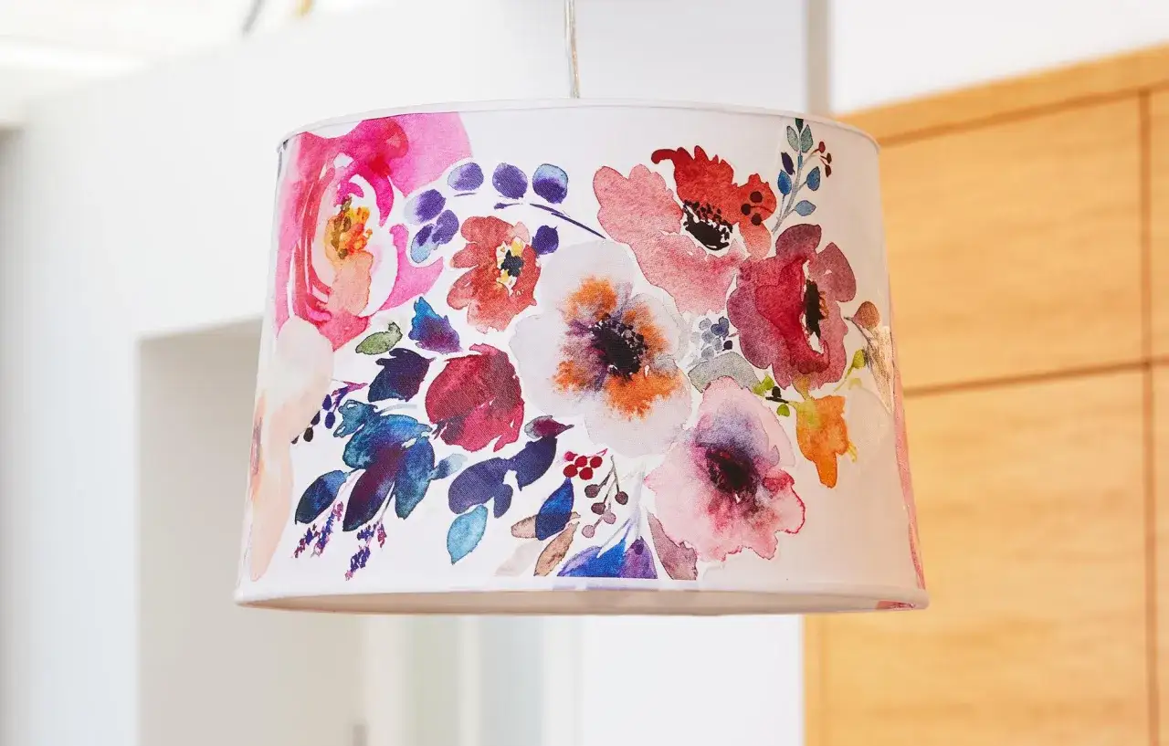 Un abat-jour suspendu, décoré de fleurs peintes à l'aquarelle dans des tons roses, rouges et bleus. Idéal pour refaire un abat-jour et apporter une touche florale.