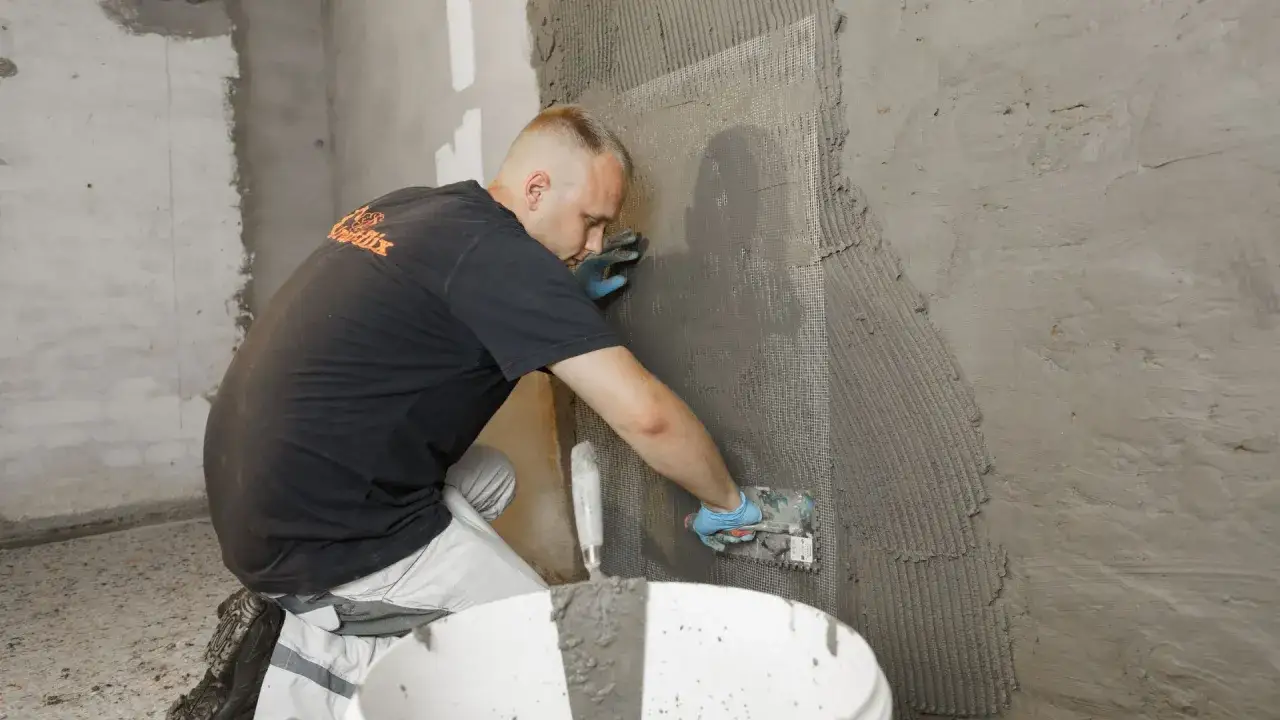 Handwerker tr&auml;gt M&ouml;rtel auf Armierungsgewebe auf, um die Wand gem&auml;&szlig; der WU-Richtlinie zu verputzen.
