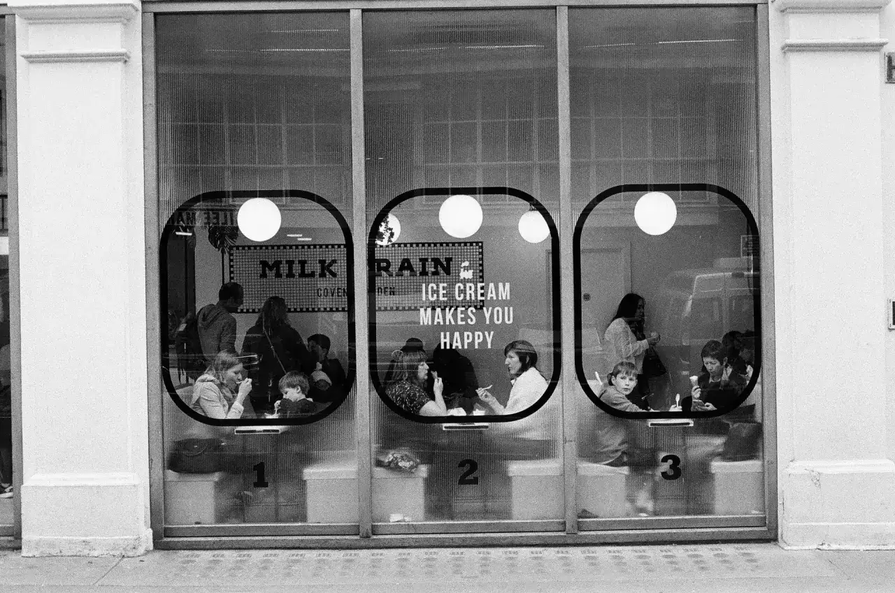 35mm street photography captures people enjoying ice cream in a shop window, with a sign proclaiming
