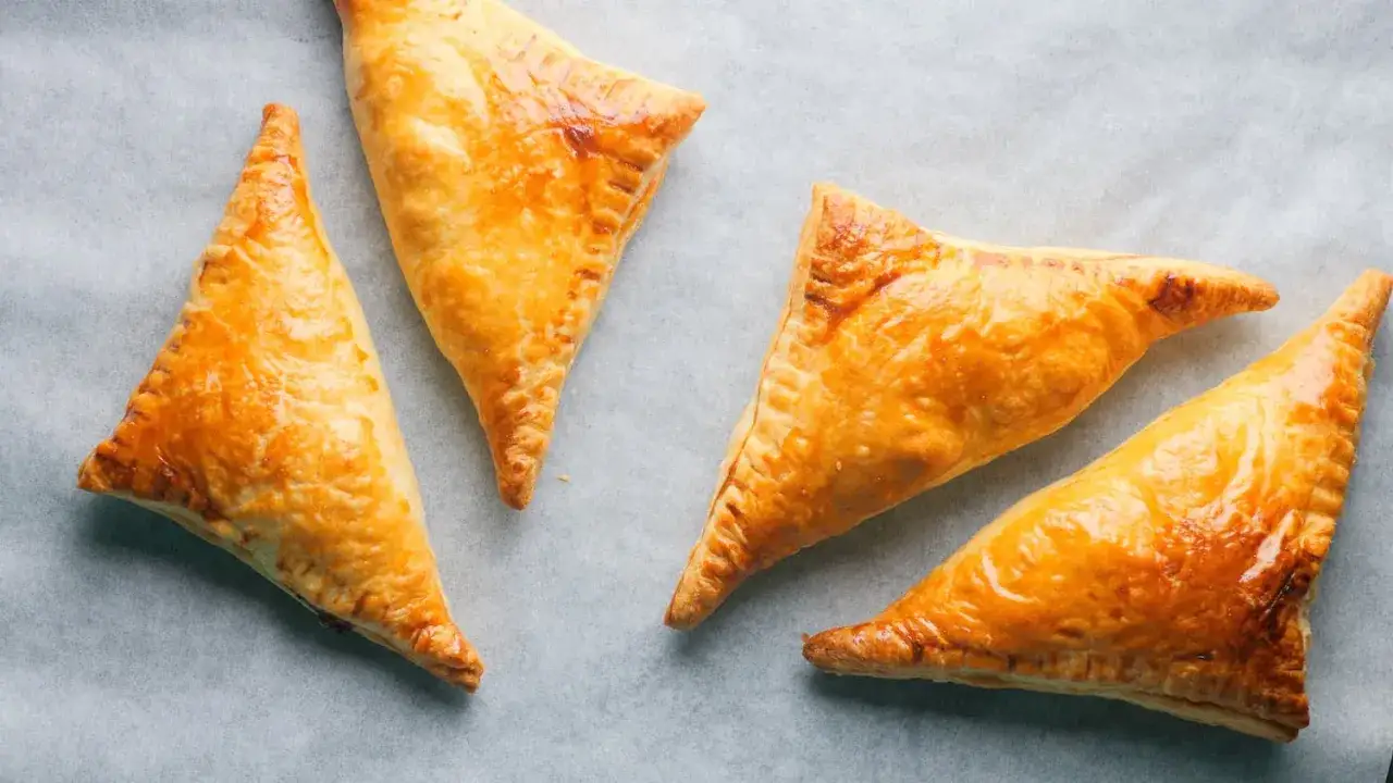 Gyldene, trekantede pastelitos de pollo ligger p&aring; bakepapir.