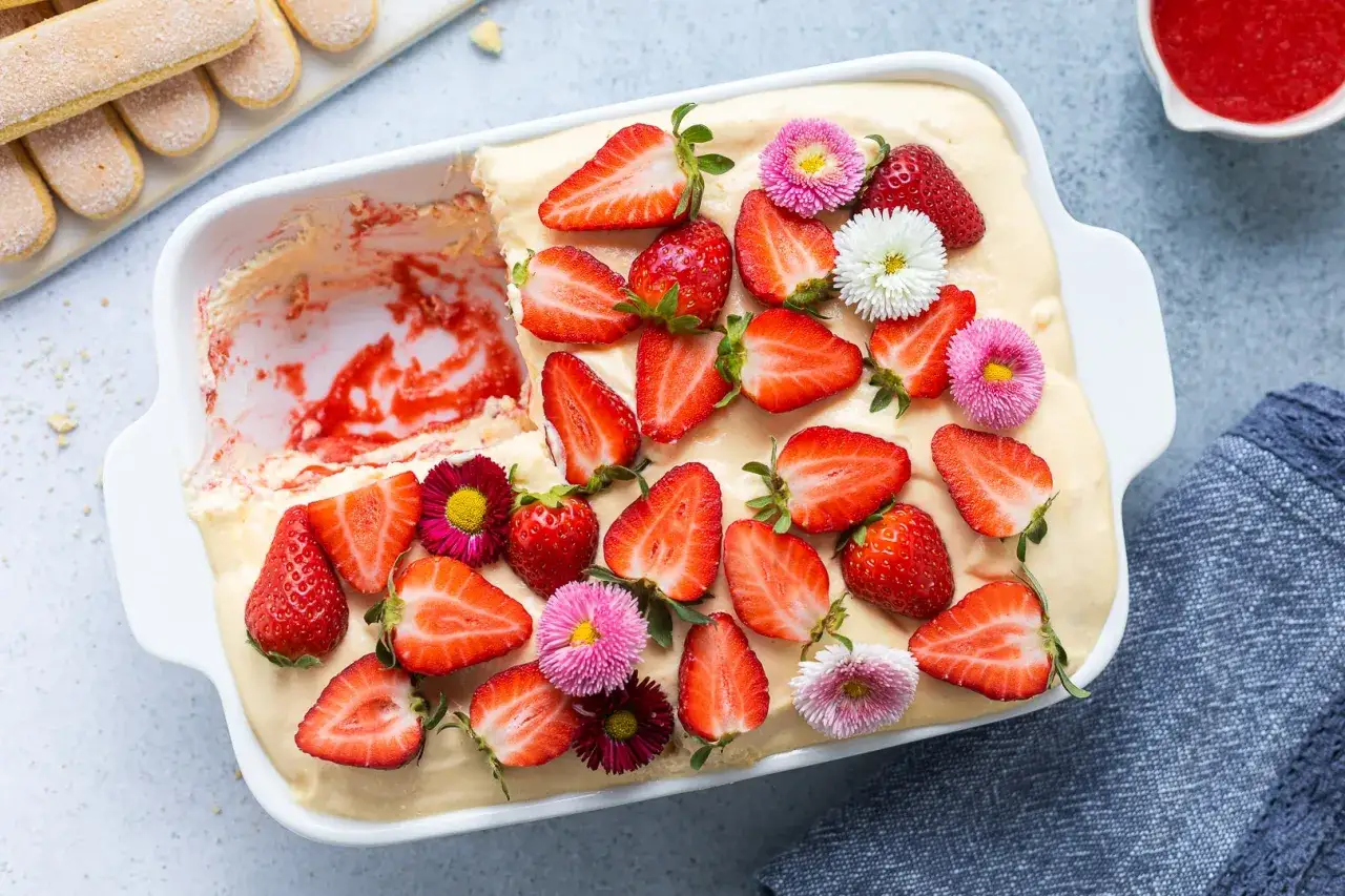 Tiramisù alle fragole ricetta originale: un dolce fresco e goloso, decorato con fragole fresche e fiori colorati.