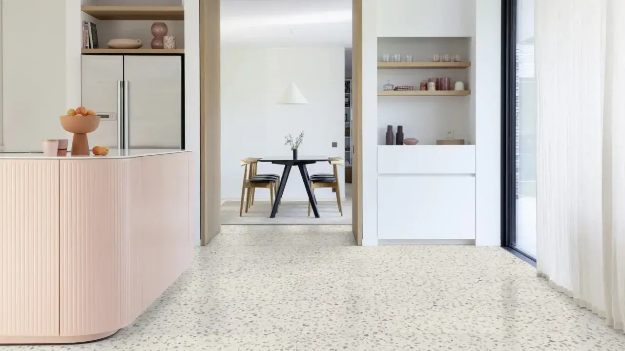 Nowoczesna kuchnia z różową zabudową i jadalnią w tle. Podłoga w delikatne wzory, która budzi pytanie: czy panele winylowe są szkodliwe?