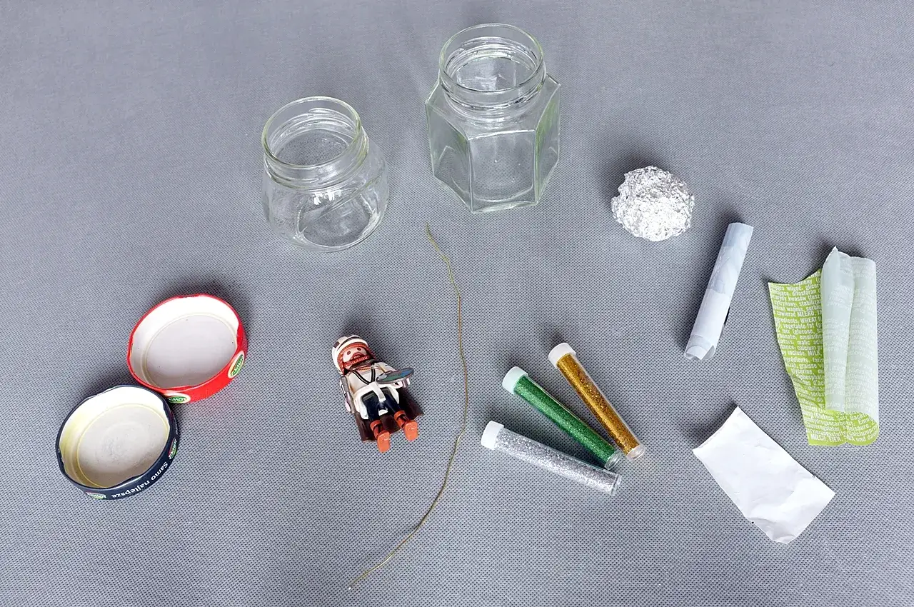 Materiały do stworzenia własnej kuli śnieżnej diy: słoiczki, figurka, brokat, drucik i folia aluminiowa.