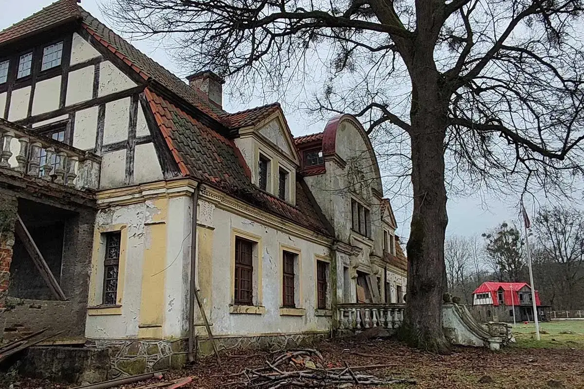 Zniszczony dworek w Paraszyne, z charakterystyczną architekturą i opadającą fasadą, otoczony jesiennym krajobrazem.
