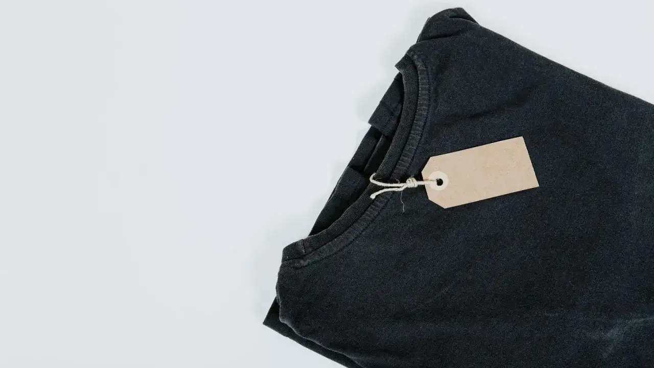 Camiseta negra doblada con etiqueta de cart&oacute;n, lista para vender ropa por internet.