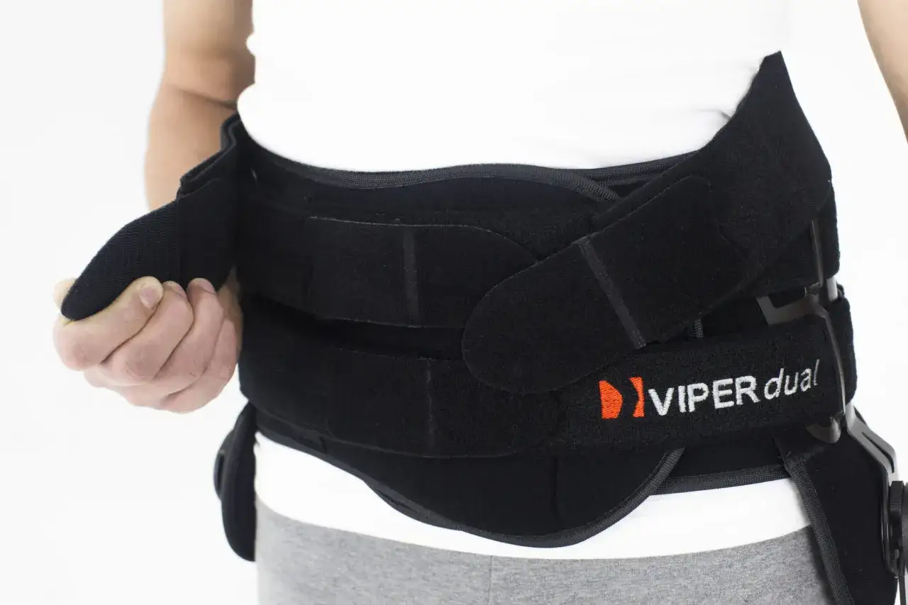 Osoba zapina czarną ortezę lędźwiową Viper Dual. To wsparcie dla kręgosłupa.