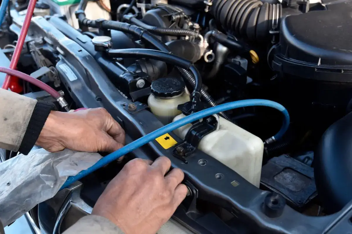 Mechanik pracuje przy silniku, podłączając węże do klimatyzacji. Czy gaz z klimatyzacji jest szkodliwy dla zdrowia?