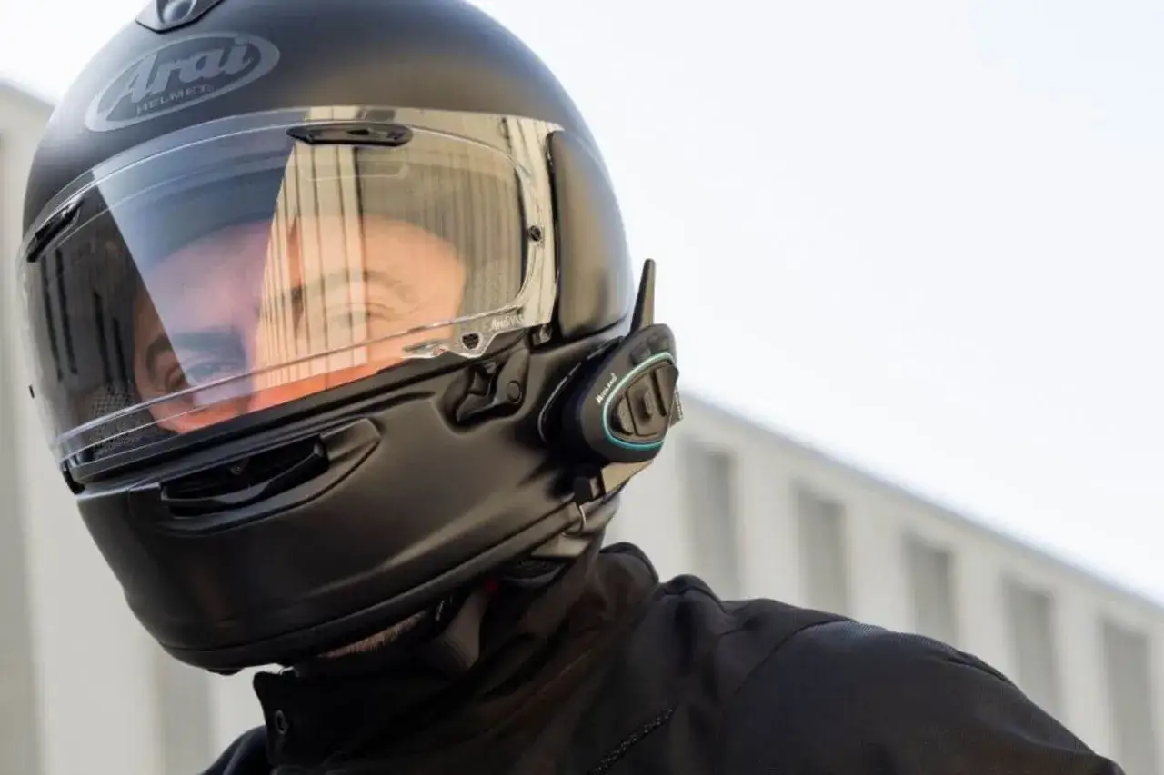 Casco de moto negro con un intercomunicador legal instalado. Reflejo del conductor en la visera.