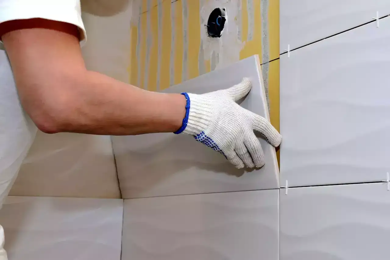 Man con guantes coloca una baldosa nueva sobre un alicatado existente.