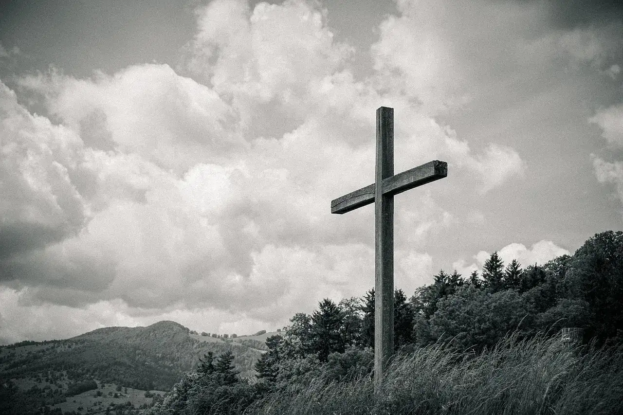 Drewniany krzyż na tle chmur i gór. Symbol nadziei i pytania, gdzie trafia dusza po śmierci.