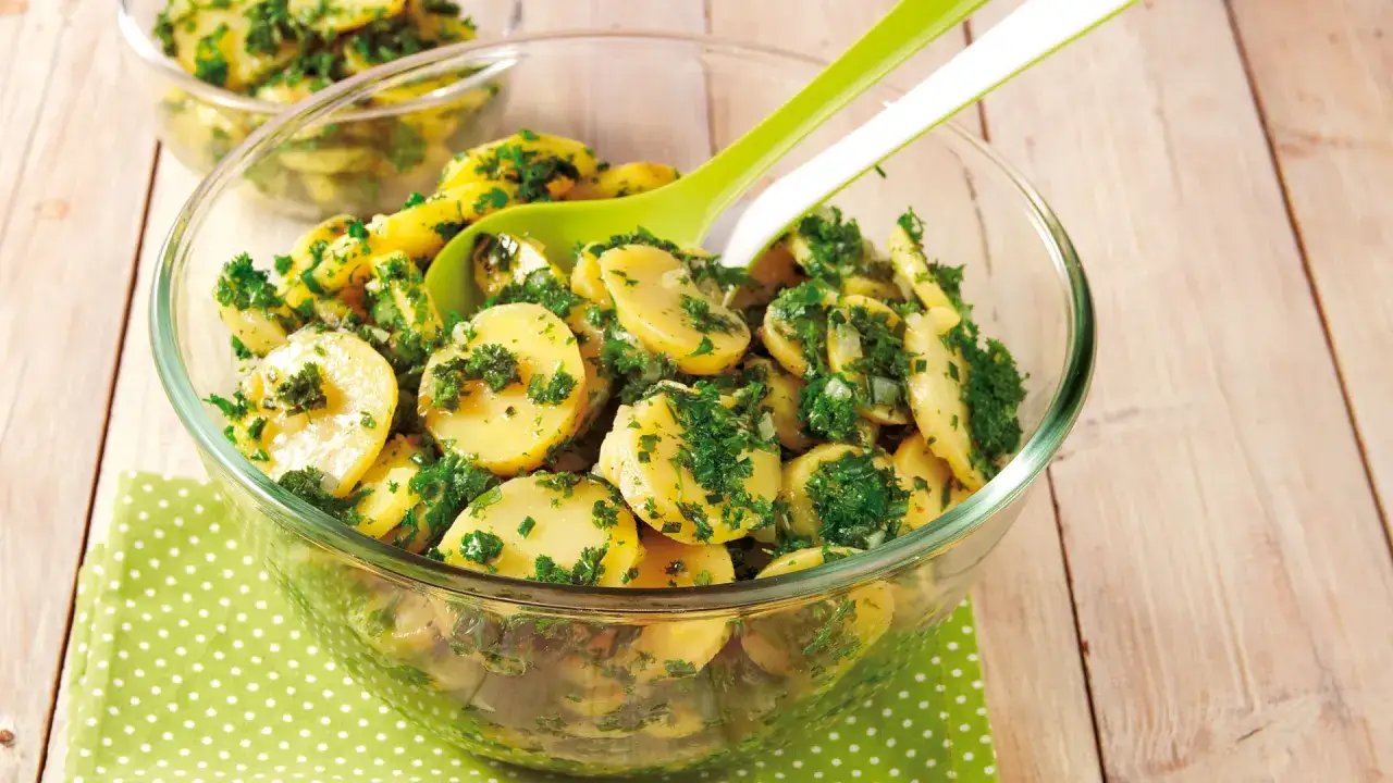 Ein köstlicher Kartoffelsalat mit Schale, verfeinert mit frischer Petersilie und Zwiebeln, serviert in einer Glasschüssel.