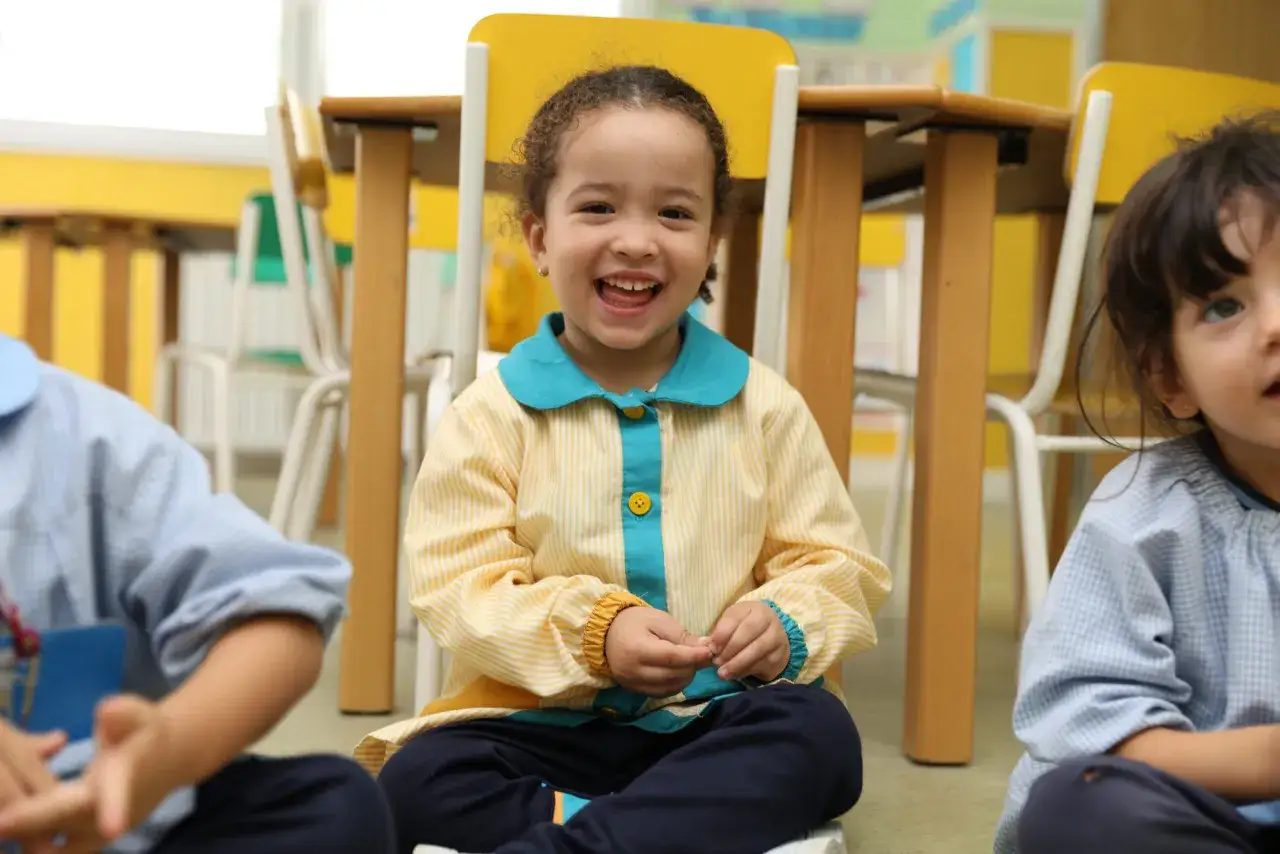 Niña sonriente en clase, aprendiendo frases positivas para niños de infantil.