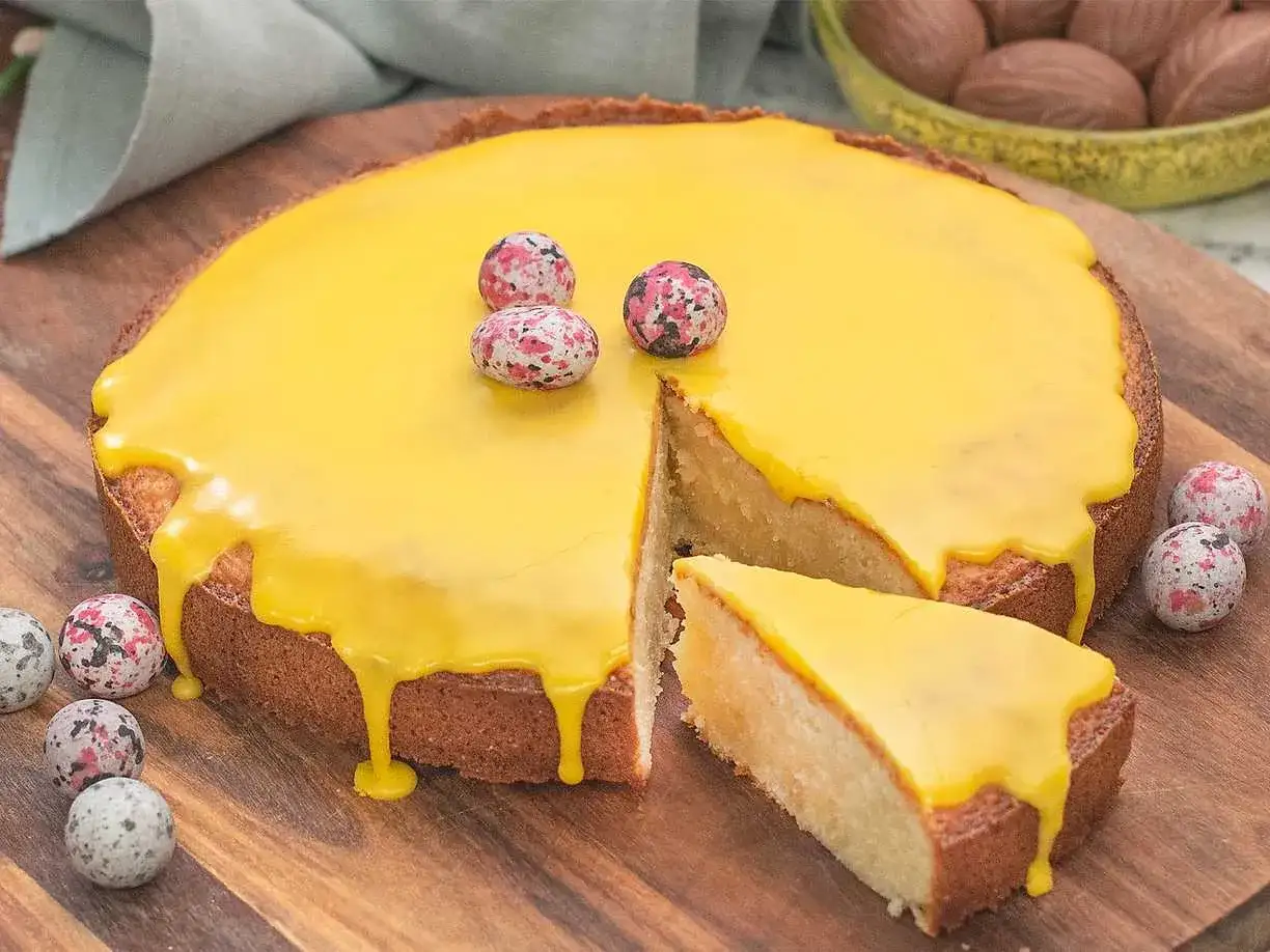 En saftig mandelkaka med citron, täckt av gul glasyr och dekorerad med små, färgglada chokladägg.